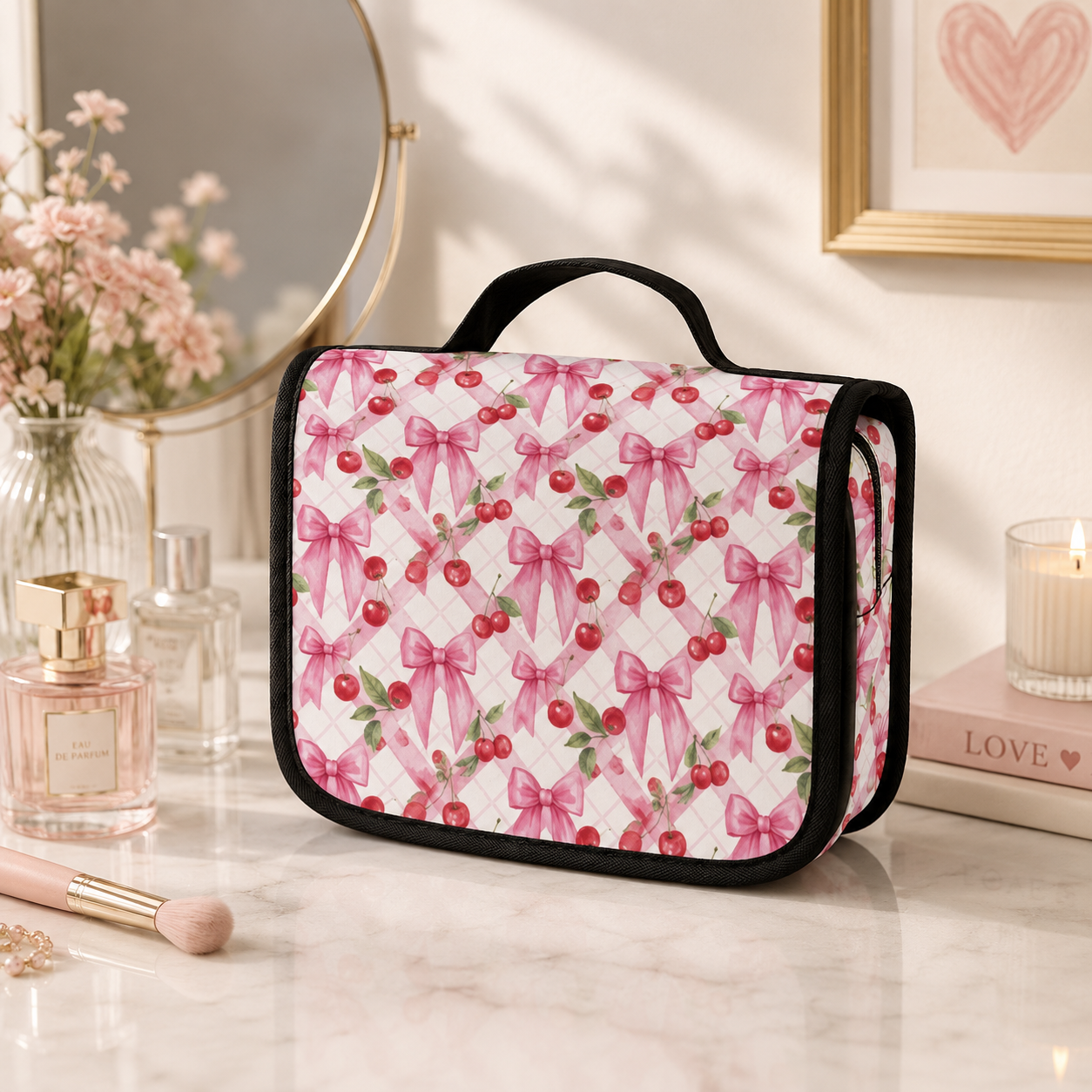 Cherry Bow pink toiletry bag with cherry and ribbon print displayed on a softly styled dressing table with perfume and flowers