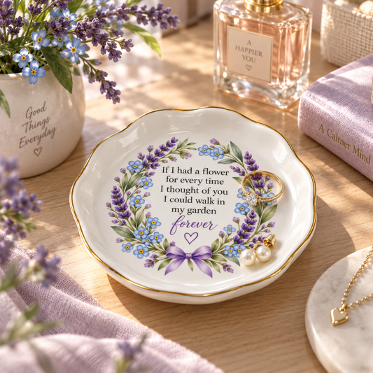 A ceramic jewelry tray with a floral wreath design and a sentimental quote, styled on a wooden table with lavender flowers, a perfume bottle, and a book in the background.