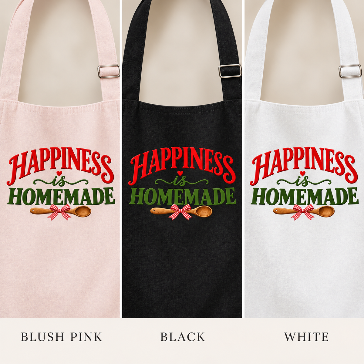 Three apron color options shown side by side: blush pink, black, and white. Each apron has the phrase “HAPPINESS is HOMEMADE” in red and green lettering with a small red-and-white bow and wooden spoon graphic.